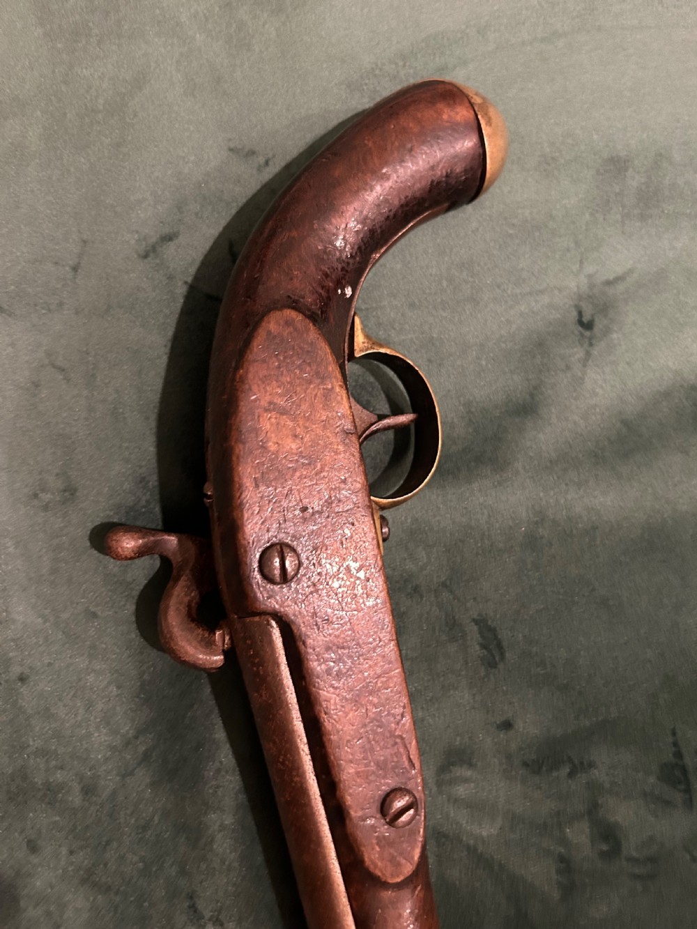 An antique single-barrel percussion pistol featuring a carved walnut stock, a metal hammer mechanism, and brass fittings along the trigger guard and butt cap. View V