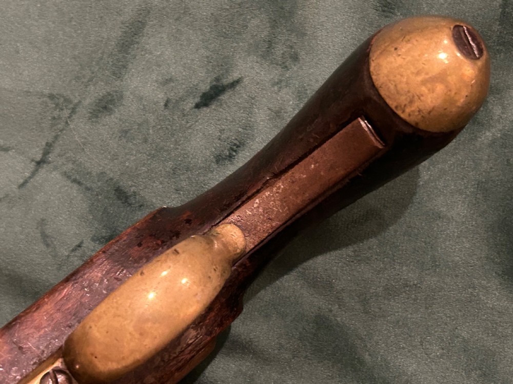 An antique single-barrel percussion pistol featuring a carved walnut stock, a metal hammer mechanism, and brass fittings along the trigger guard and butt cap. View VIII