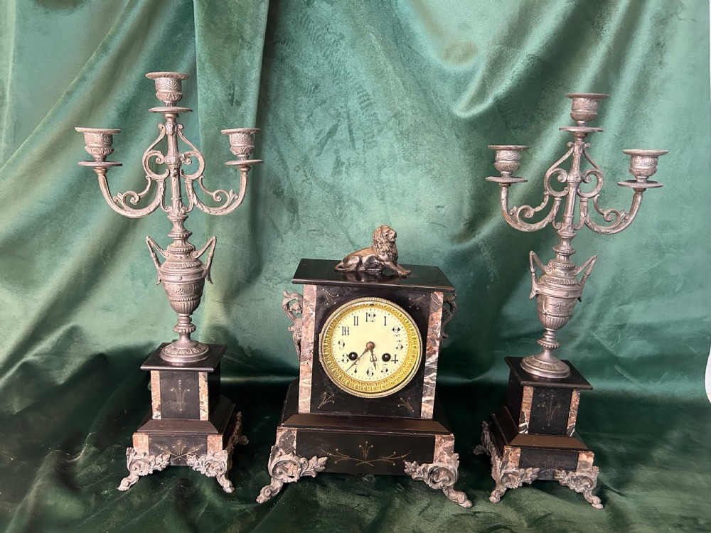 A three-piece French black slate clock garniture set comprising a central mantel clock topped with a lion figure and flanked by two matching multi-branch candelabra.