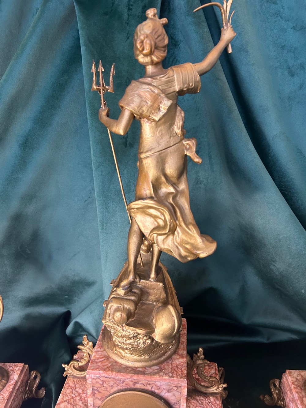 A three-piece French clock garniture set featuring a central mantel clock topped with a gilded classical figure on a pink marble base, flanked by two matching gilded side urns. View II