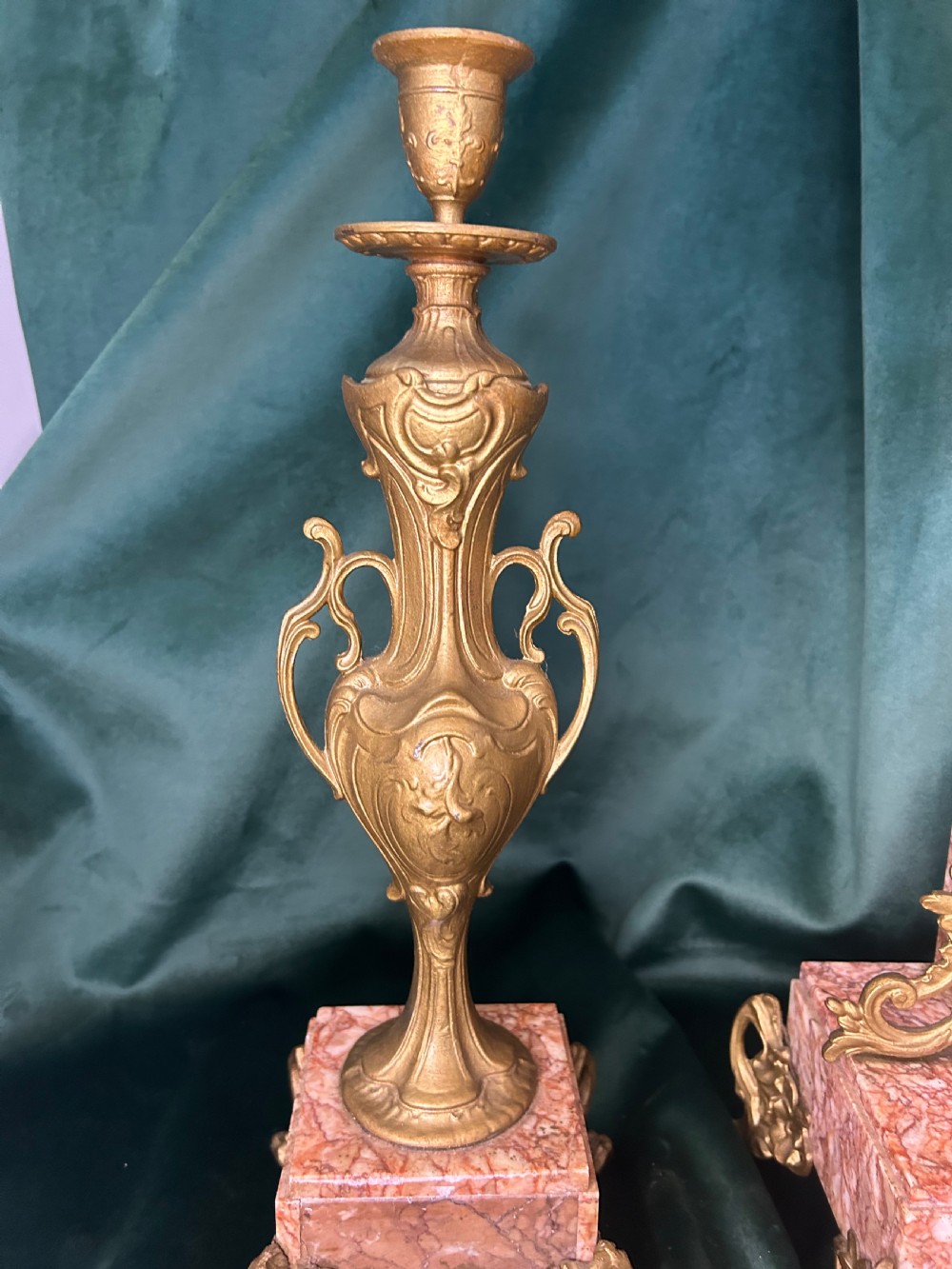A three-piece French clock garniture set featuring a central mantel clock topped with a gilded classical figure on a pink marble base, flanked by two matching gilded side urns. View IV