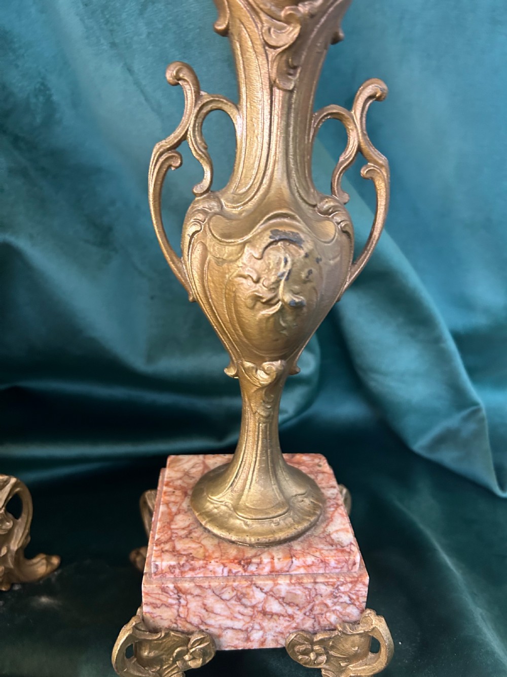 A three-piece French clock garniture set featuring a central mantel clock topped with a gilded classical figure on a pink marble base, flanked by two matching gilded side urns. View VII