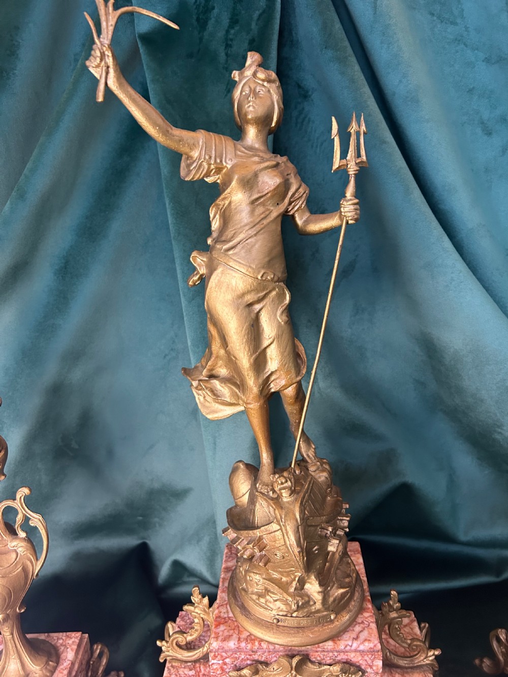 A three-piece French clock garniture set featuring a central mantel clock topped with a gilded classical figure on a pink marble base, flanked by two matching gilded side urns. View IX