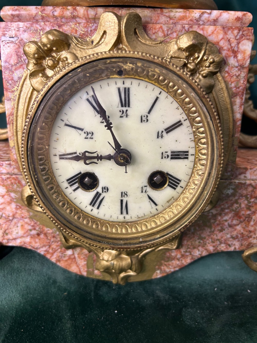 A three-piece French clock garniture set featuring a central mantel clock topped with a gilded classical figure on a pink marble base, flanked by two matching gilded side urns. View X