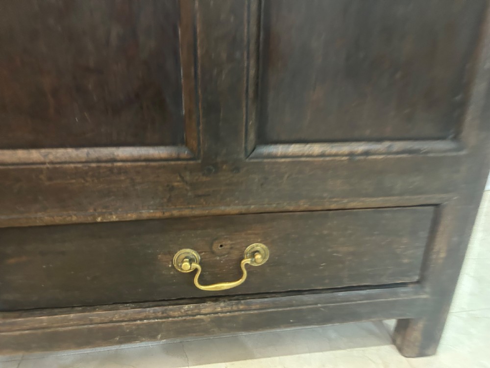 An 18th-century dark oak mule chest featuring a four-panel front, two base drawers with brass handles, and a hinged lid. View V