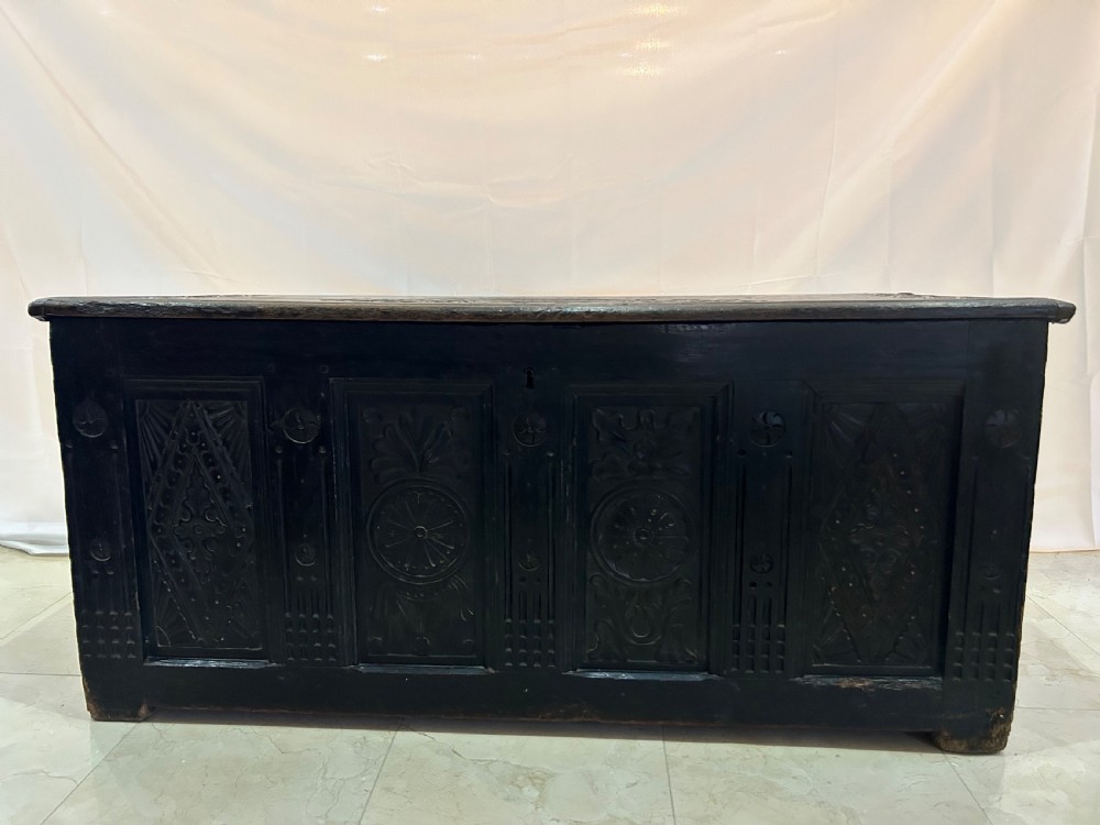 A dark carved wooden antique coffer featuring four rectangular front panels decorated with geometric lozenge and rosette motifs.