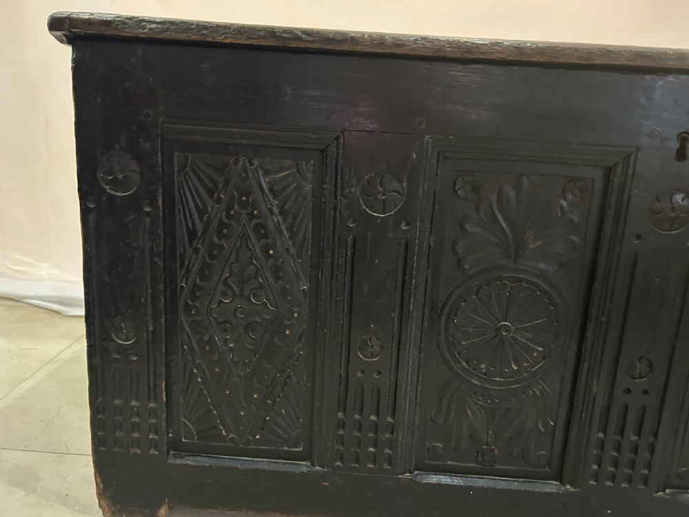 A dark carved wooden antique coffer featuring four rectangular front panels decorated with geometric lozenge and rosette motifs. View III