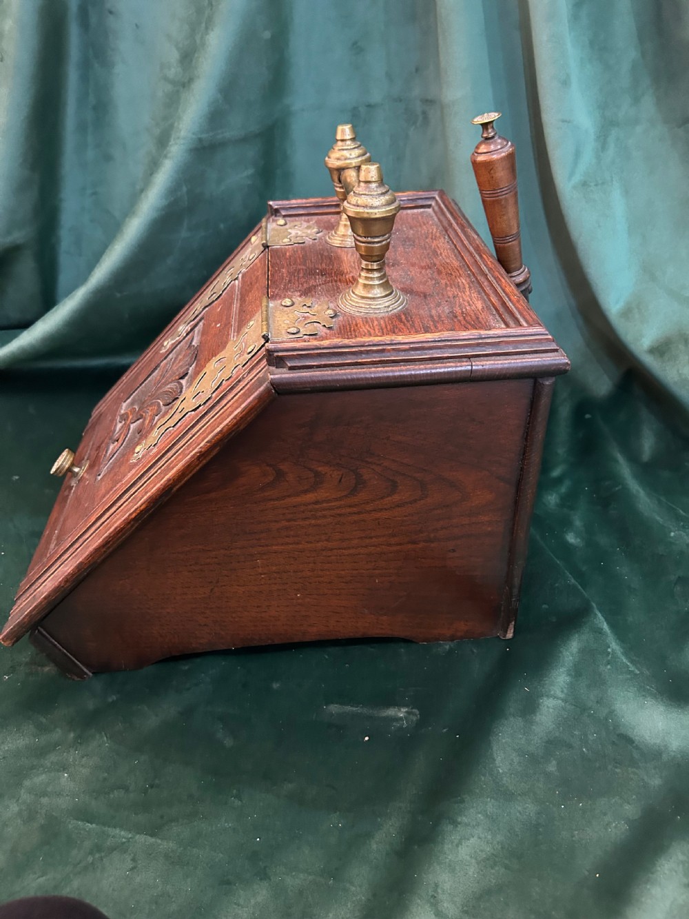 An antique dark oak wooden coal box with sloped lid, carved leaf panel, brass carrying handle, and ornate brass hinges. View II