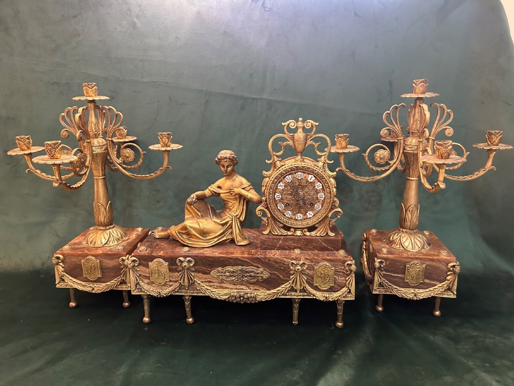 An antique three-piece French ormolu clock garniture featuring a central mantel clock decorated with a classical female figurine and marble base, flanked by two matching five-arm candelabra.