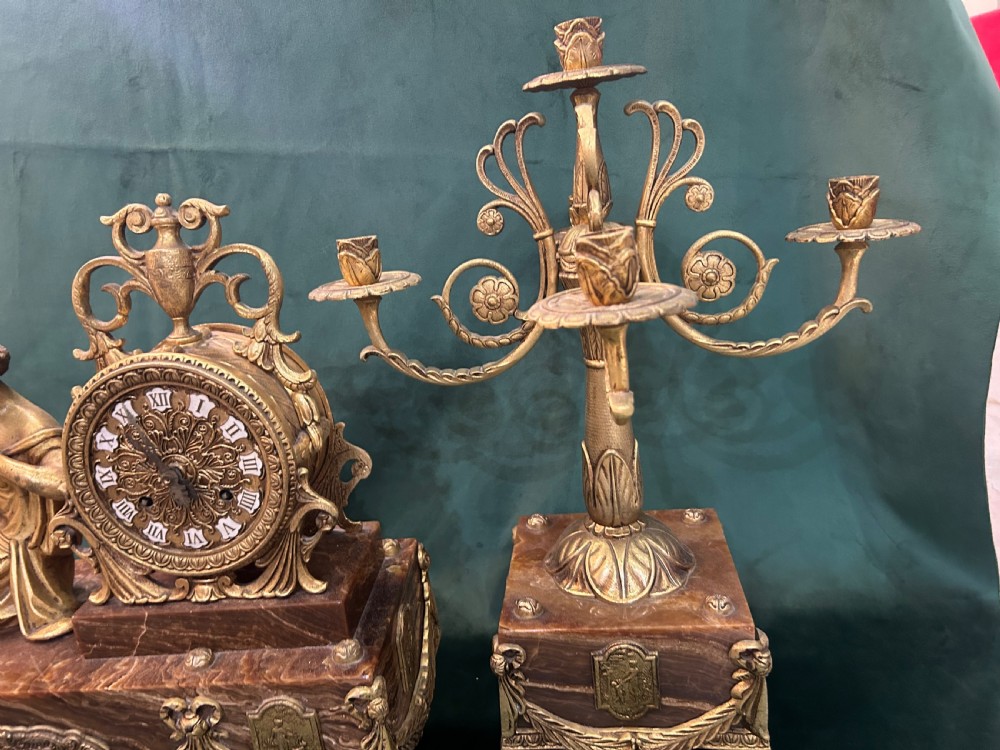 An antique three-piece French ormolu clock garniture featuring a central mantel clock decorated with a classical female figurine and marble base, flanked by two matching five-arm candelabra. View III
