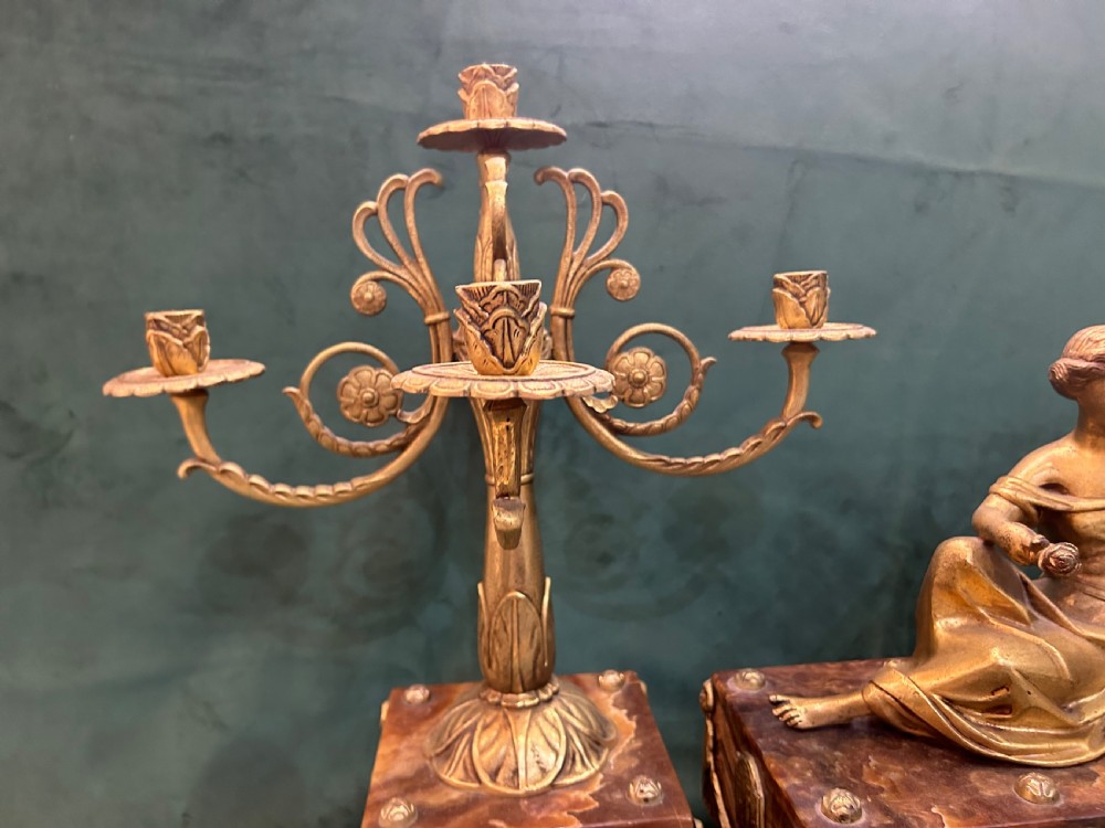 An antique three-piece French ormolu clock garniture featuring a central mantel clock decorated with a classical female figurine and marble base, flanked by two matching five-arm candelabra. View VI
