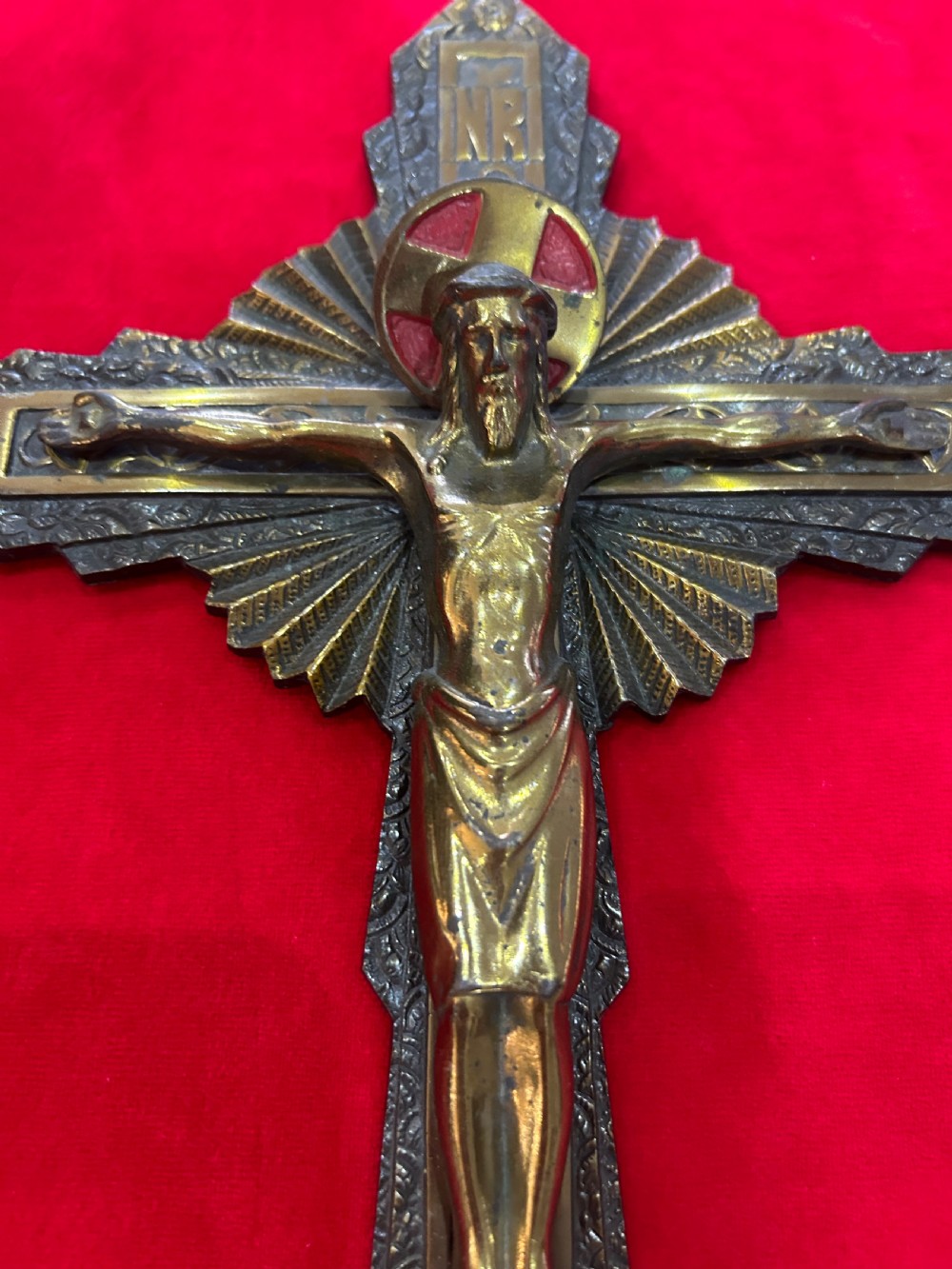 An Art Deco brass crucifix featuring a geometric cross structure with a sunburst halo, red enamelled accents, and a relief figure of Christ. View II