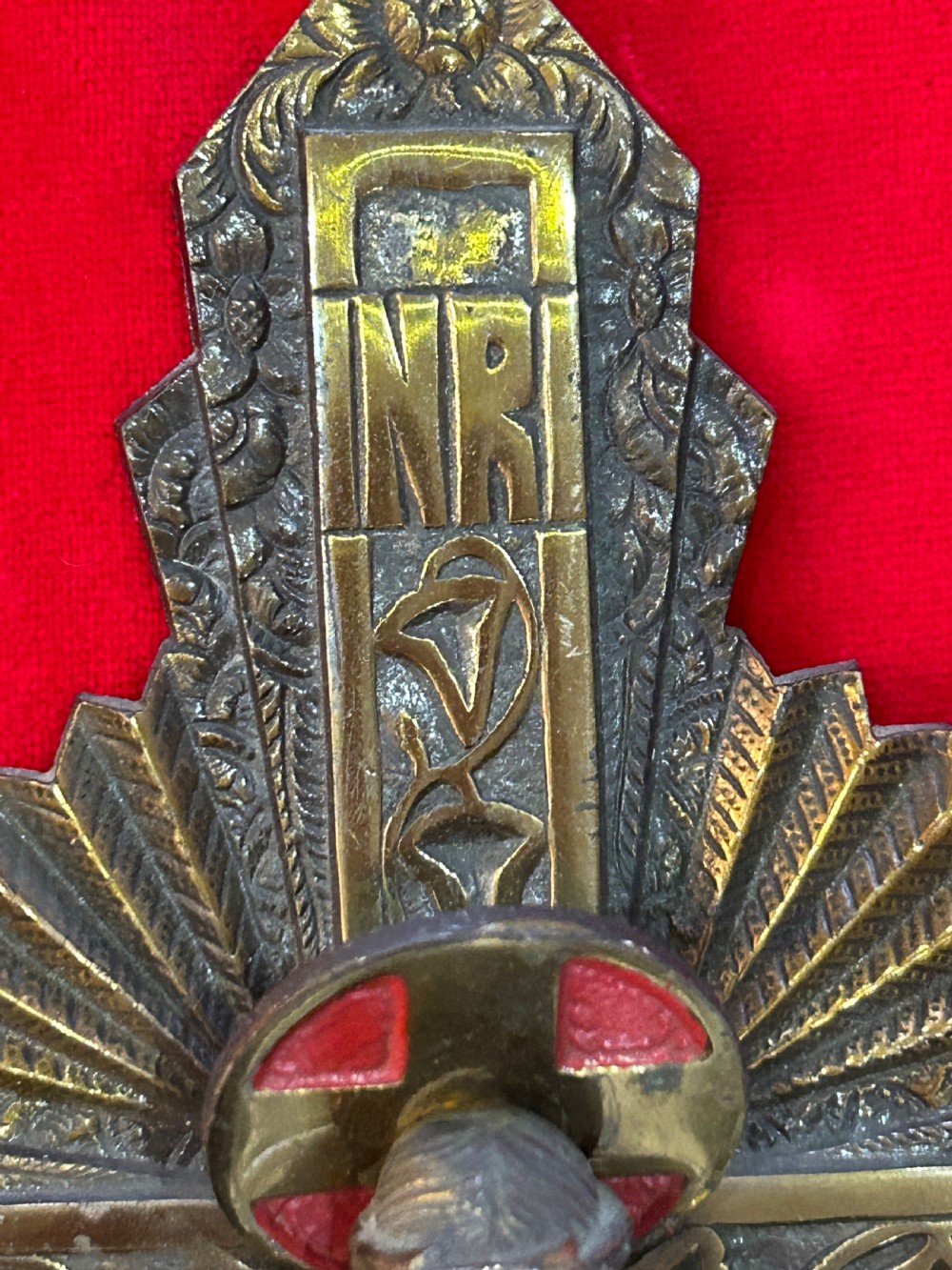 An Art Deco brass crucifix featuring a geometric cross structure with a sunburst halo, red enamelled accents, and a relief figure of Christ. View V