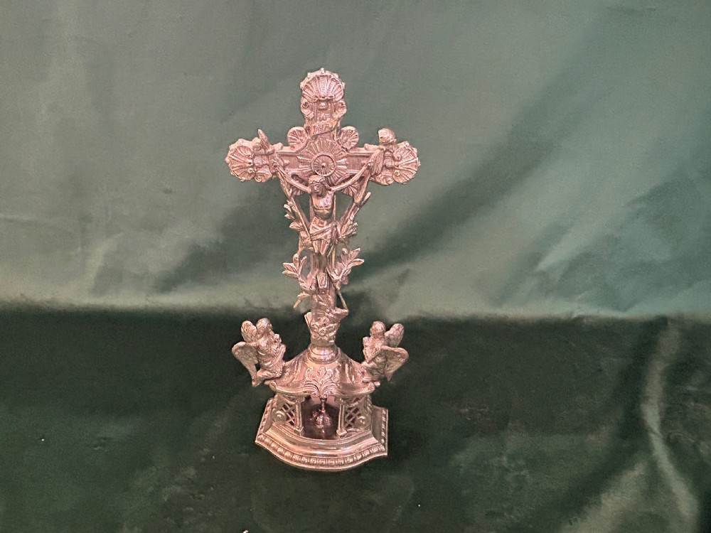 An antique silver metal standing altar cross featuring shell motif terminals, a figure of Christ, and two kneeling angels on a moulded pedestal base.