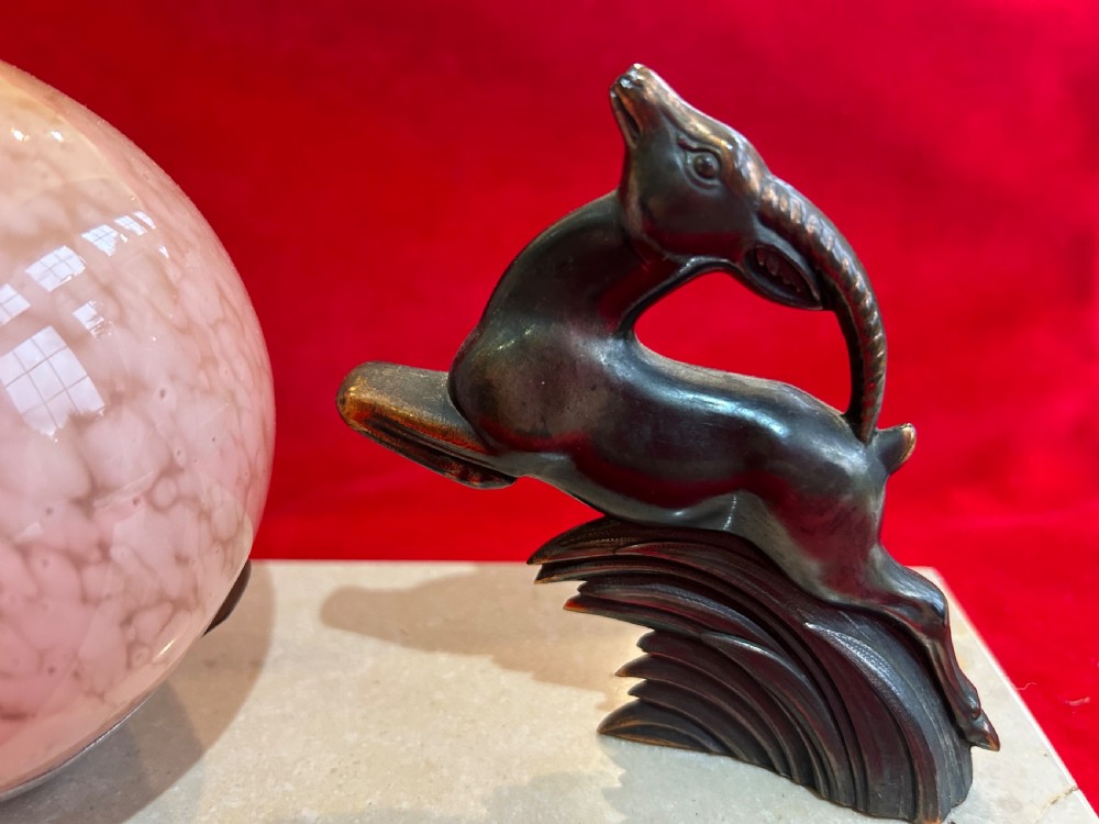 An Art Deco table lamp featuring a rectangular beige marble base, a cast metal leaping gazelle figurine, and a spherical mottled pink glass globe shade. View II
