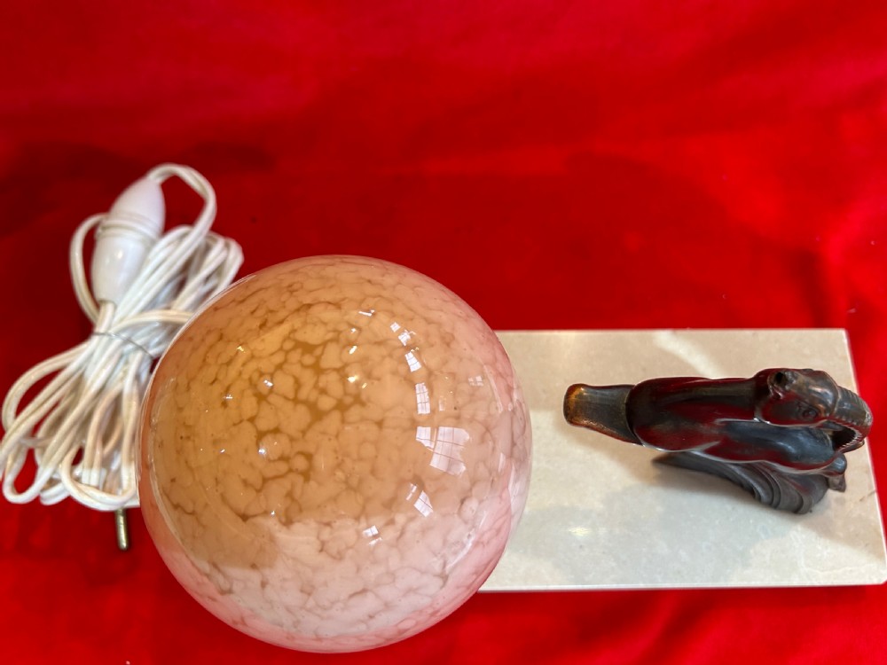 An Art Deco table lamp featuring a rectangular beige marble base, a cast metal leaping gazelle figurine, and a spherical mottled pink glass globe shade. View V