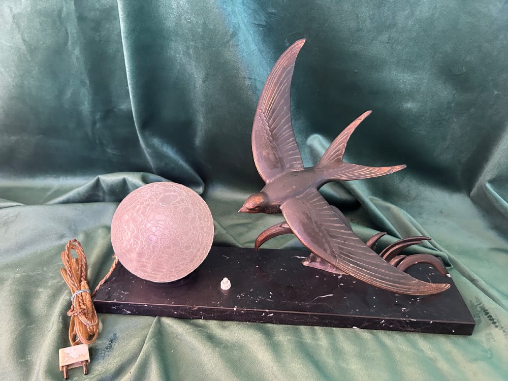 An Art Deco table lamp featuring a patinated metal bird in flight beside a spherical frosted glass globe on a black marble base.