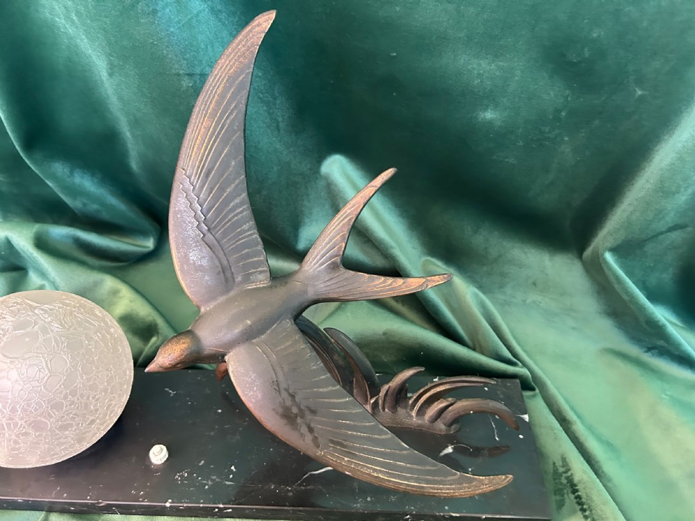 An Art Deco table lamp featuring a patinated metal bird in flight beside a spherical frosted glass globe on a black marble base. View II