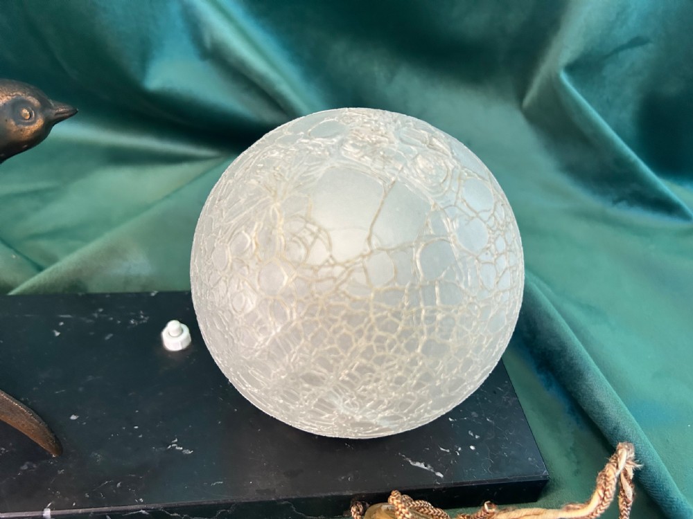 An Art Deco table lamp featuring a patinated metal bird in flight beside a spherical frosted glass globe on a black marble base. View IV