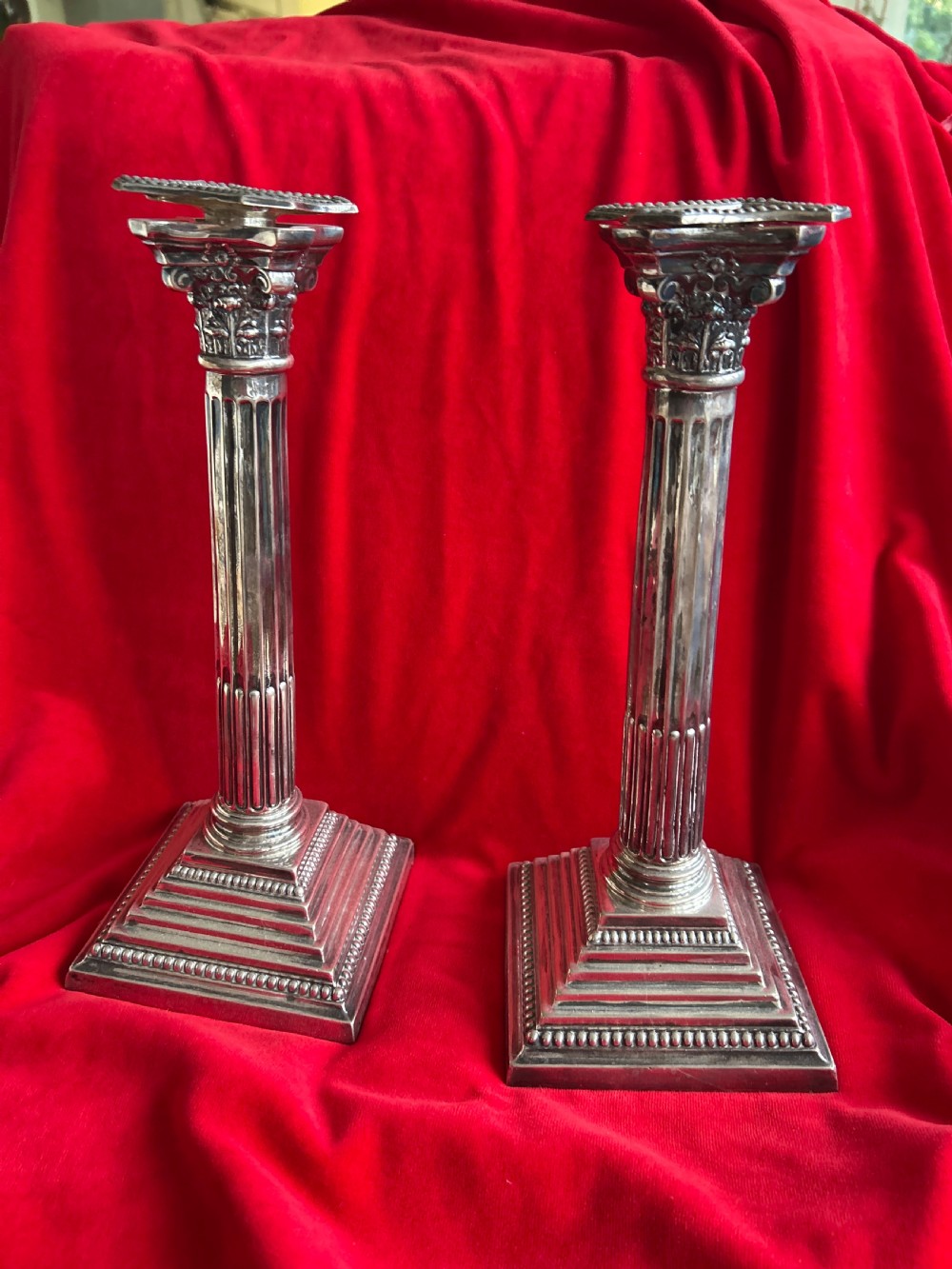 A pair of silver Neoclassical Corinthian column candlesticks featuring fluted shafts and beaded stepped square bases.