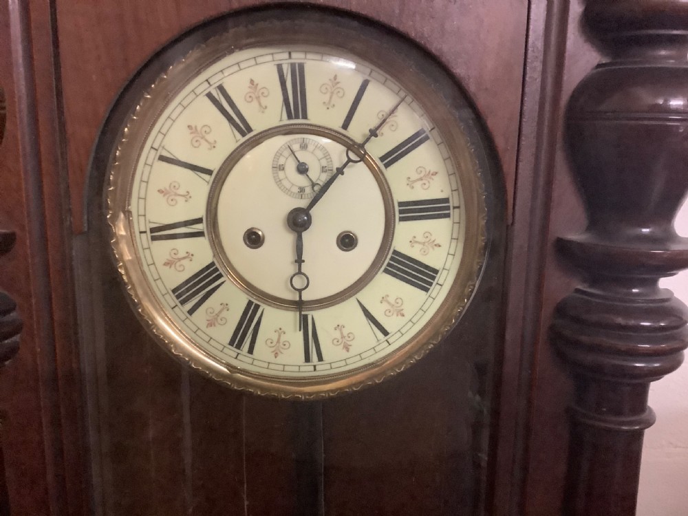 A Victorian Vienna regulator wall clock featuring a dark walnut glazed case, turned side columns, two brass weights, and a circular dial with Roman numerals. View III