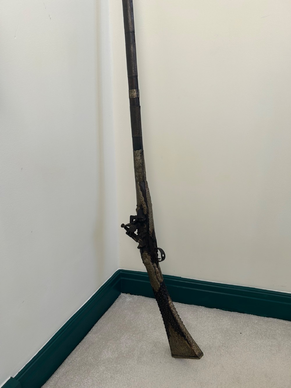 An antique Afghan flintlock Jezail rifle featuring a curved wooden stock adorned with embossed metalwork, a long iron barrel, and a traditional firing mechanism.
