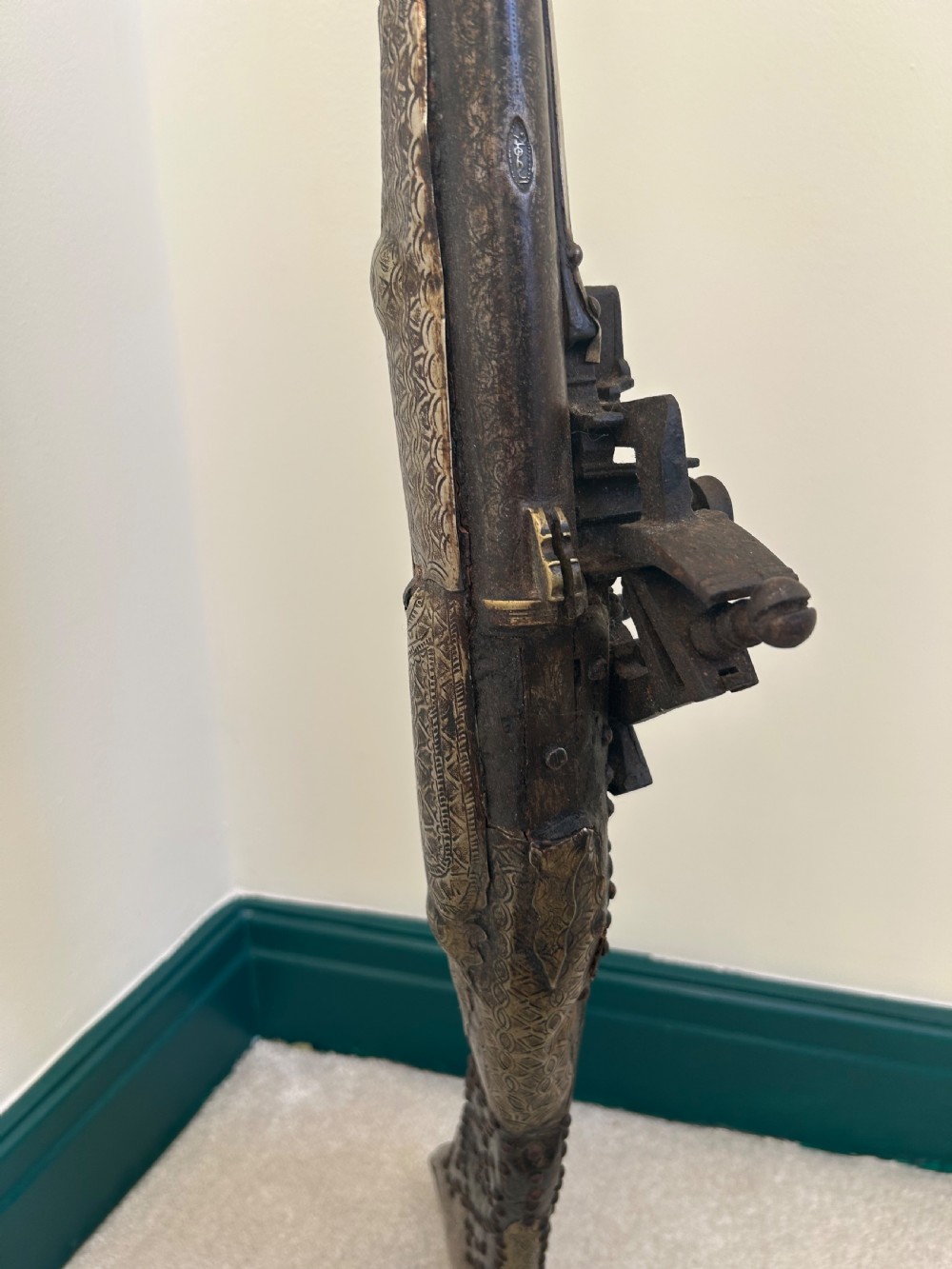 An antique Afghan flintlock Jezail rifle featuring a curved wooden stock adorned with embossed metalwork, a long iron barrel, and a traditional firing mechanism. View V