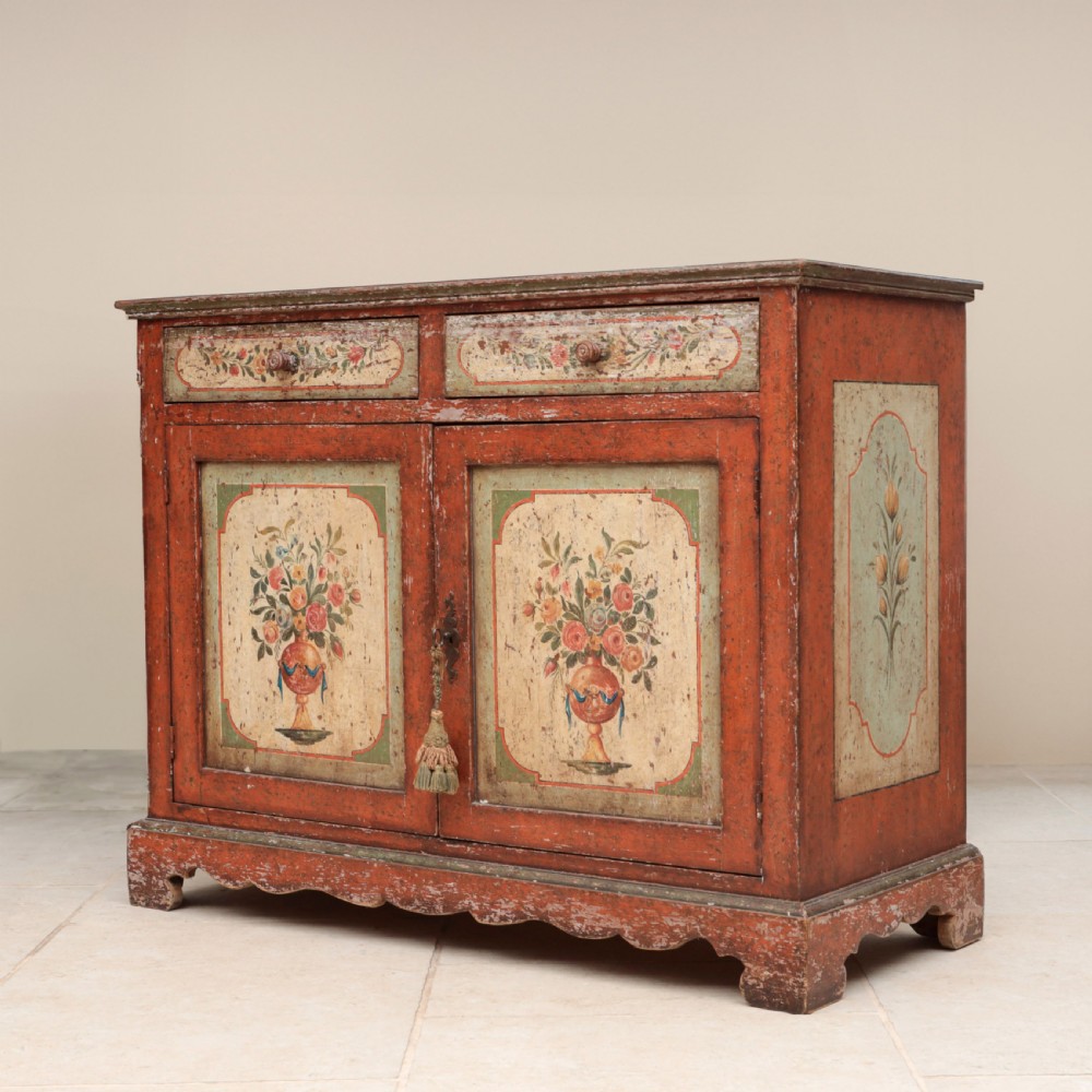 A 19th-century terracotta red painted wooden cabinet featuring two upper drawers and two cupboard doors adorned with cream panels hand-painted with floral urn designs. View II