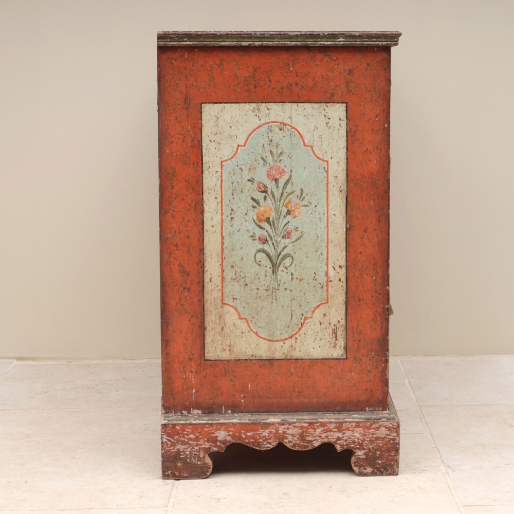 A 19th-century terracotta red painted wooden cabinet featuring two upper drawers and two cupboard doors adorned with cream panels hand-painted with floral urn designs. View VI