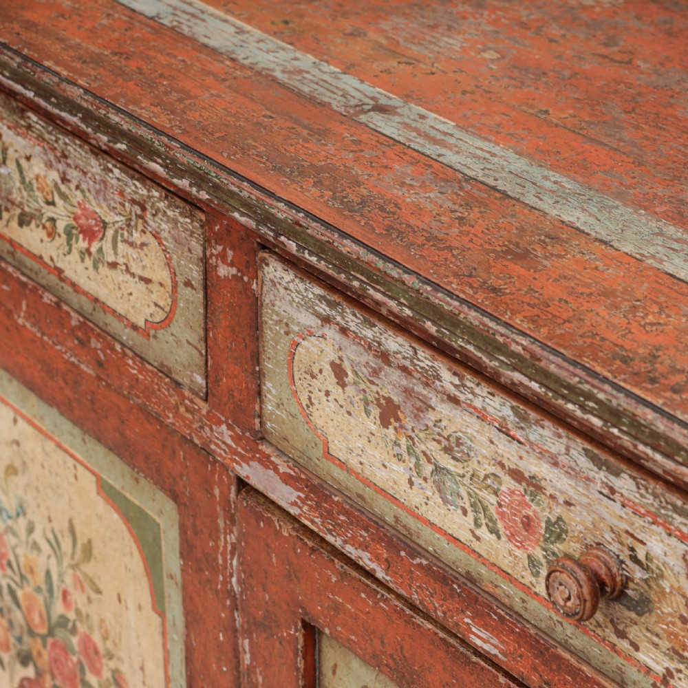A 19th-century terracotta red painted wooden cabinet featuring two upper drawers and two cupboard doors adorned with cream panels hand-painted with floral urn designs. View IX