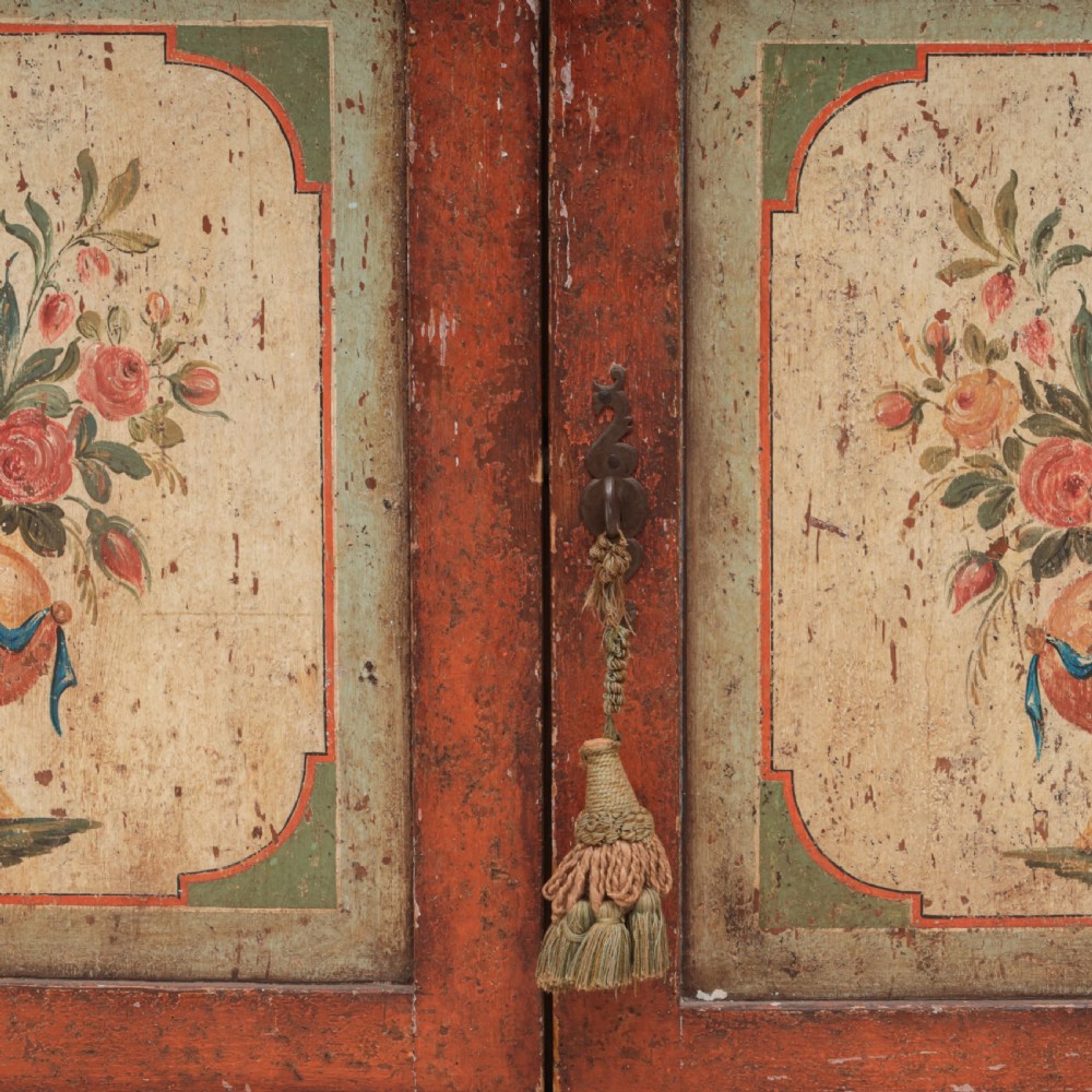 A 19th-century terracotta red painted wooden cabinet featuring two upper drawers and two cupboard doors adorned with cream panels hand-painted with floral urn designs. View X