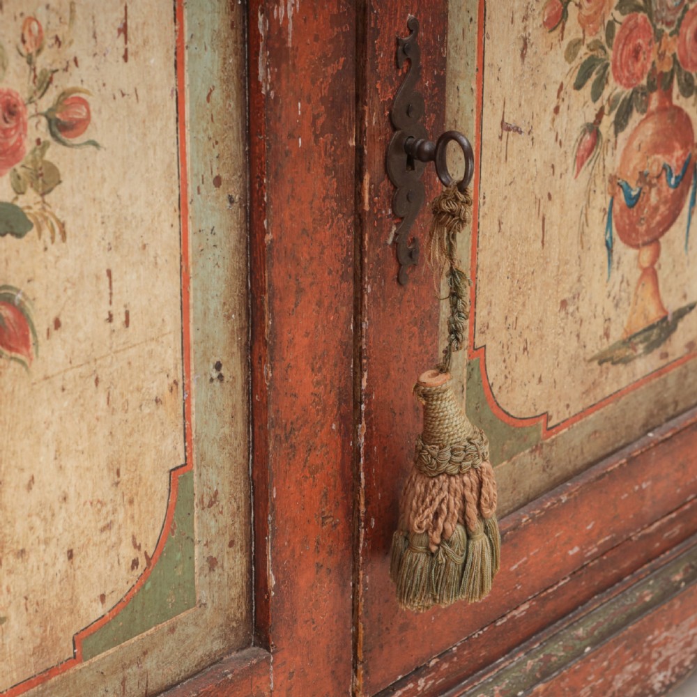 A 19th-century terracotta red painted wooden cabinet featuring two upper drawers and two cupboard doors adorned with cream panels hand-painted with floral urn designs. View XI