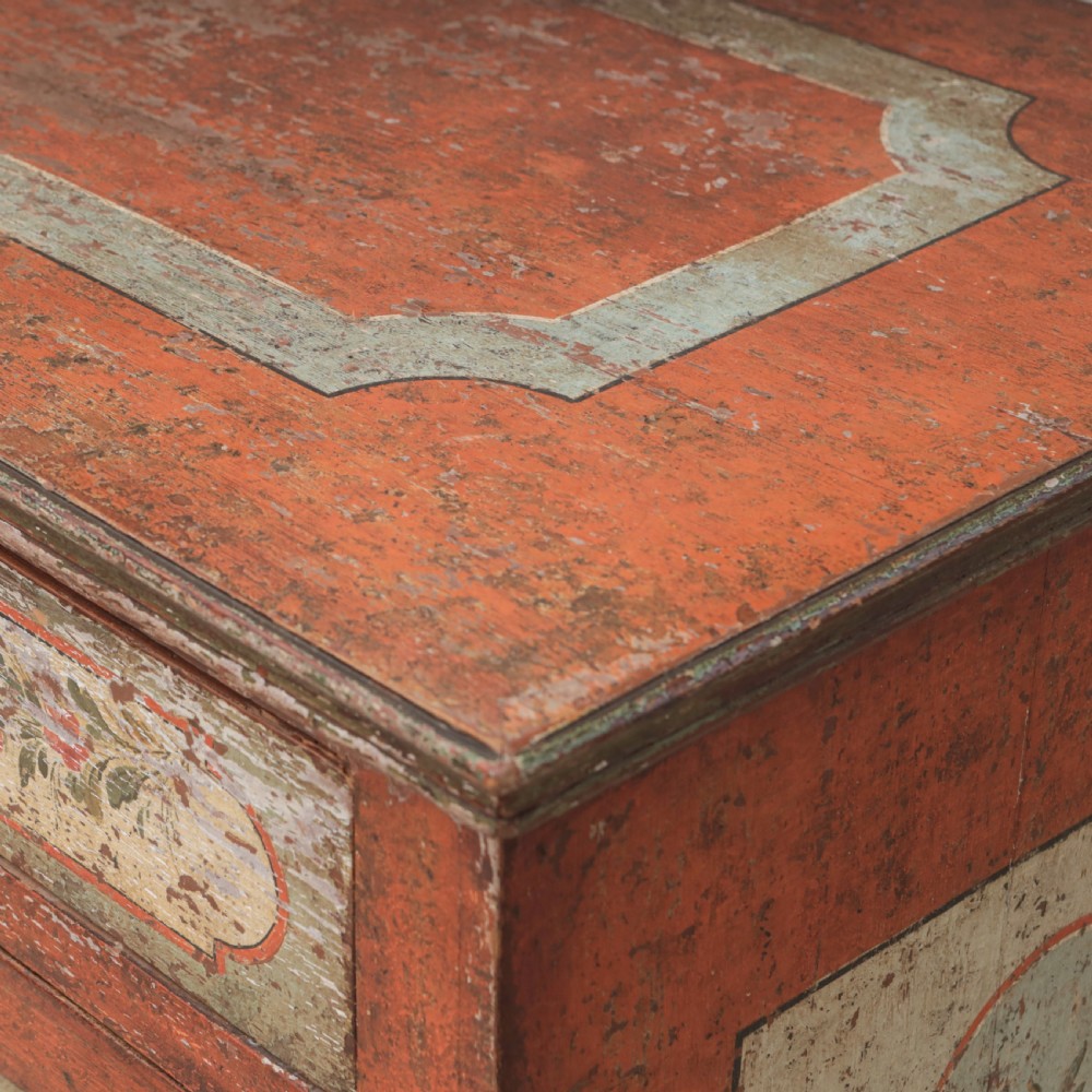 A 19th-century terracotta red painted wooden cabinet featuring two upper drawers and two cupboard doors adorned with cream panels hand-painted with floral urn designs. View XV
