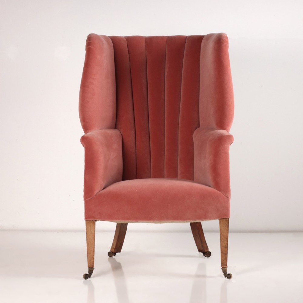 An 18th-century style barrel back armchair upholstered in dusty pink velvet with vertical channel quilting, standing on wooden legs with brass castors.