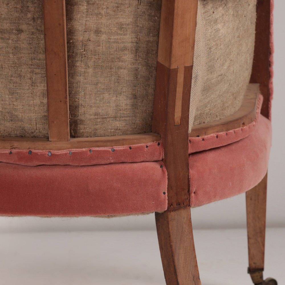 An 18th-century style barrel back armchair upholstered in dusty pink velvet with vertical channel quilting, standing on wooden legs with brass castors. View VI
