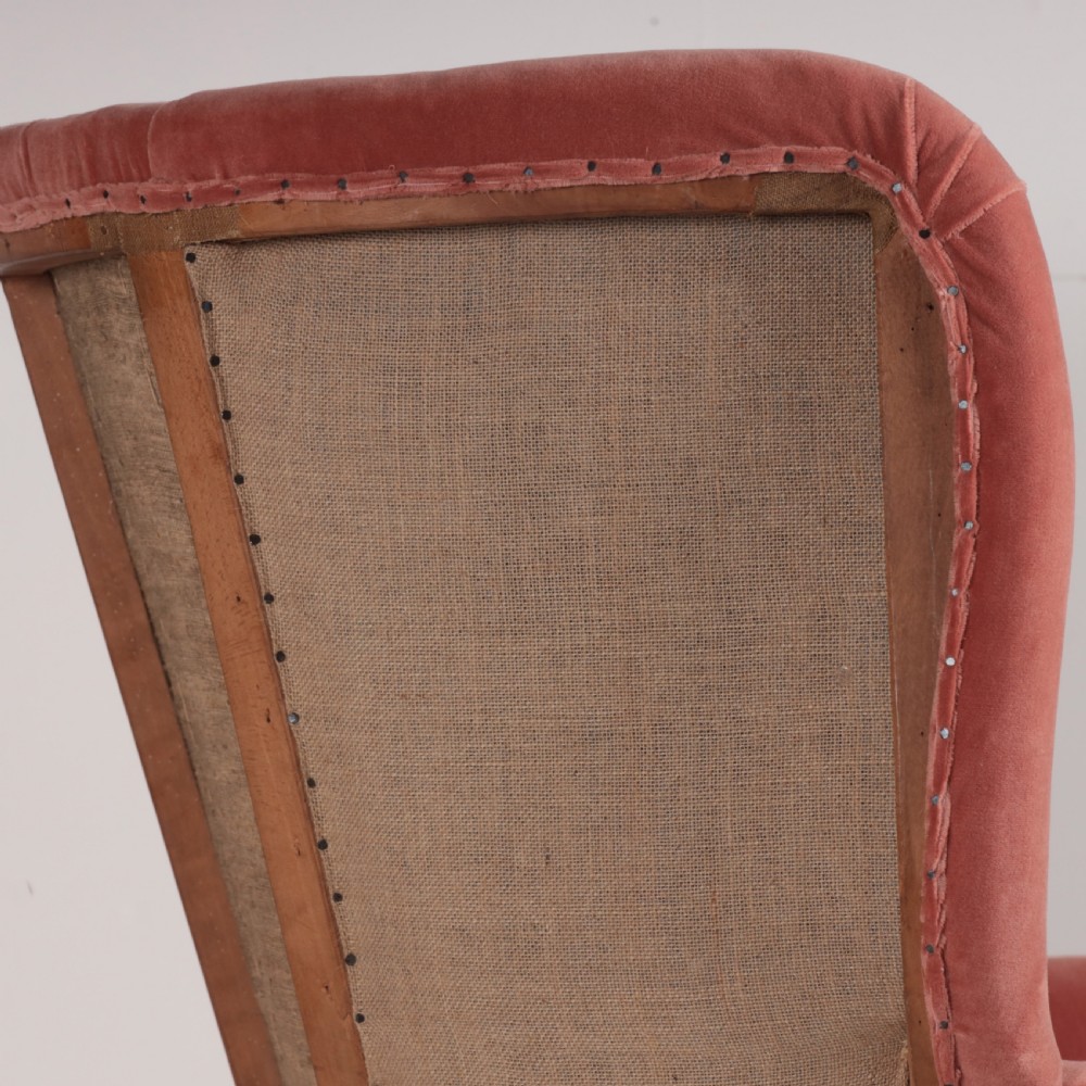 An 18th-century style barrel back armchair upholstered in dusty pink velvet with vertical channel quilting, standing on wooden legs with brass castors. View VII
