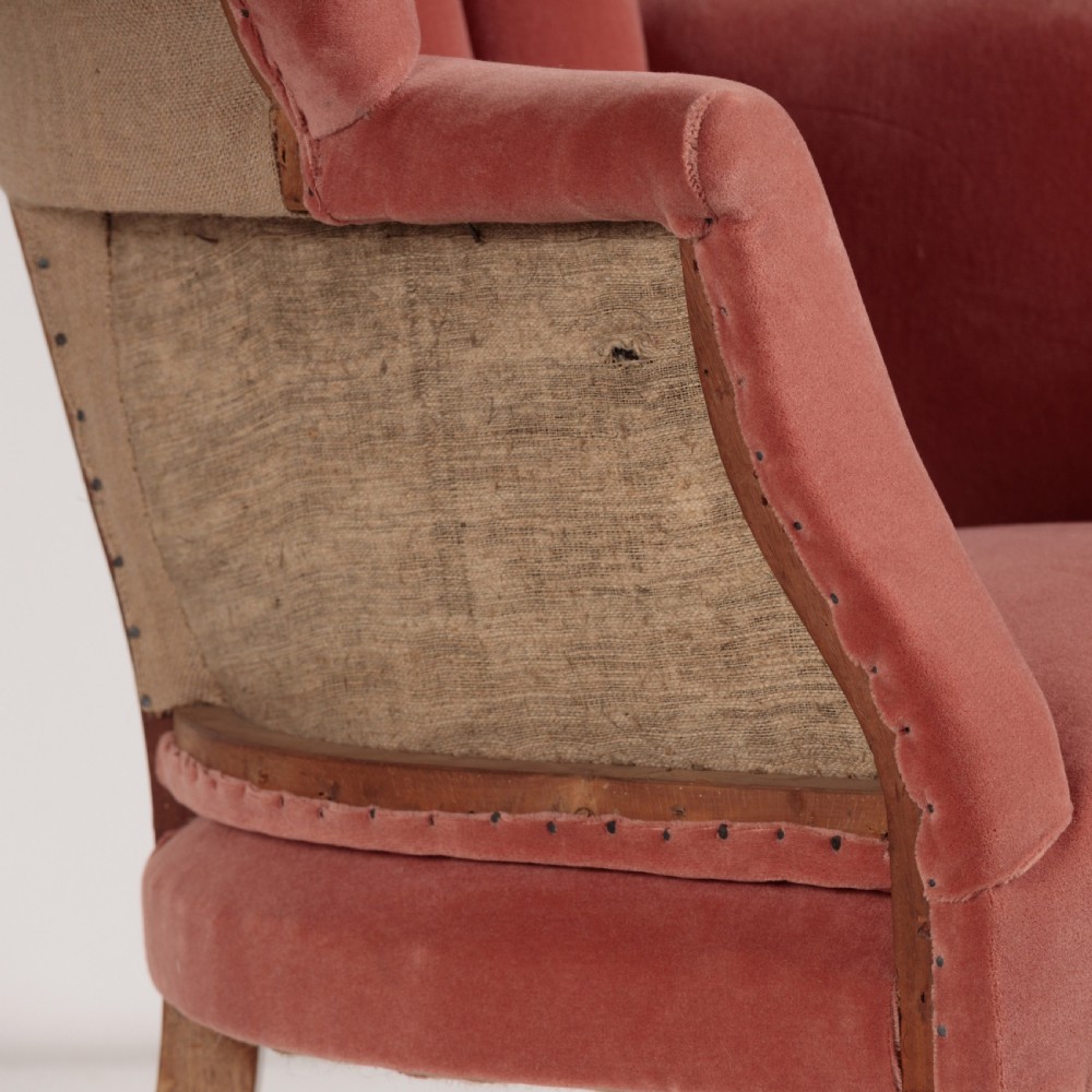 An 18th-century style barrel back armchair upholstered in dusty pink velvet with vertical channel quilting, standing on wooden legs with brass castors. View IX