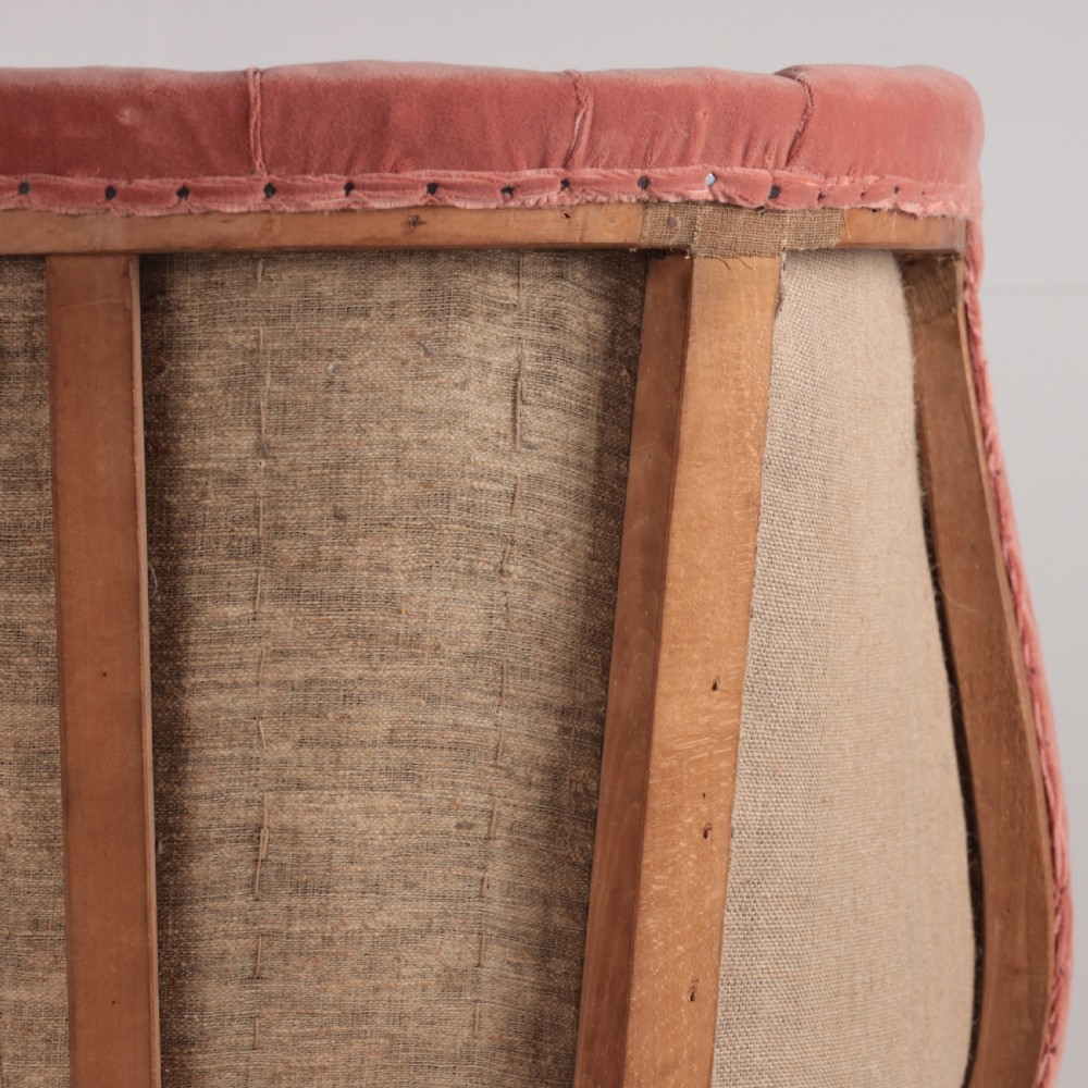 An 18th-century style barrel back armchair upholstered in dusty pink velvet with vertical channel quilting, standing on wooden legs with brass castors. View X