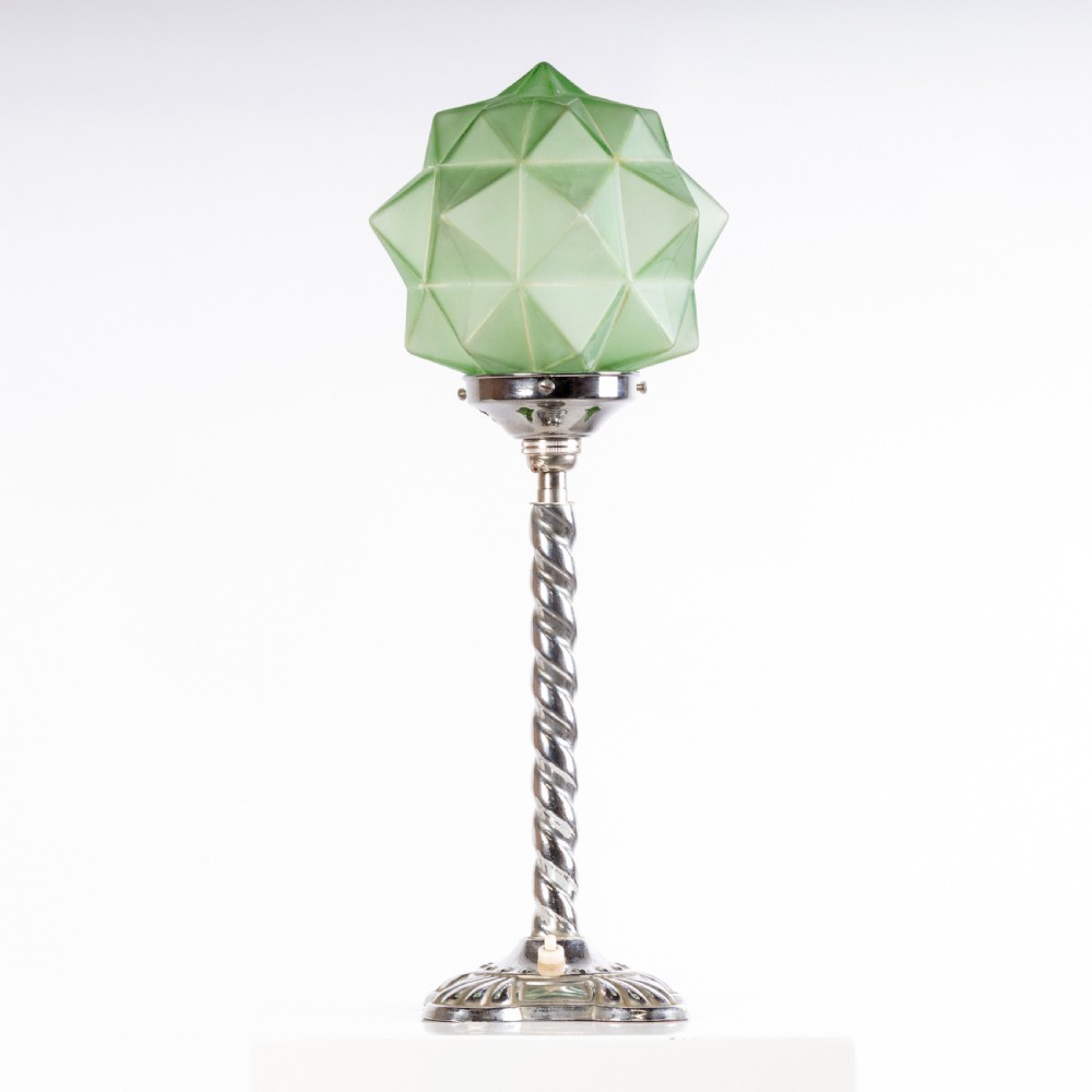 An Art Deco table lamp featuring a faceted light green frosted glass shade atop a chrome twisted stem and circular base.