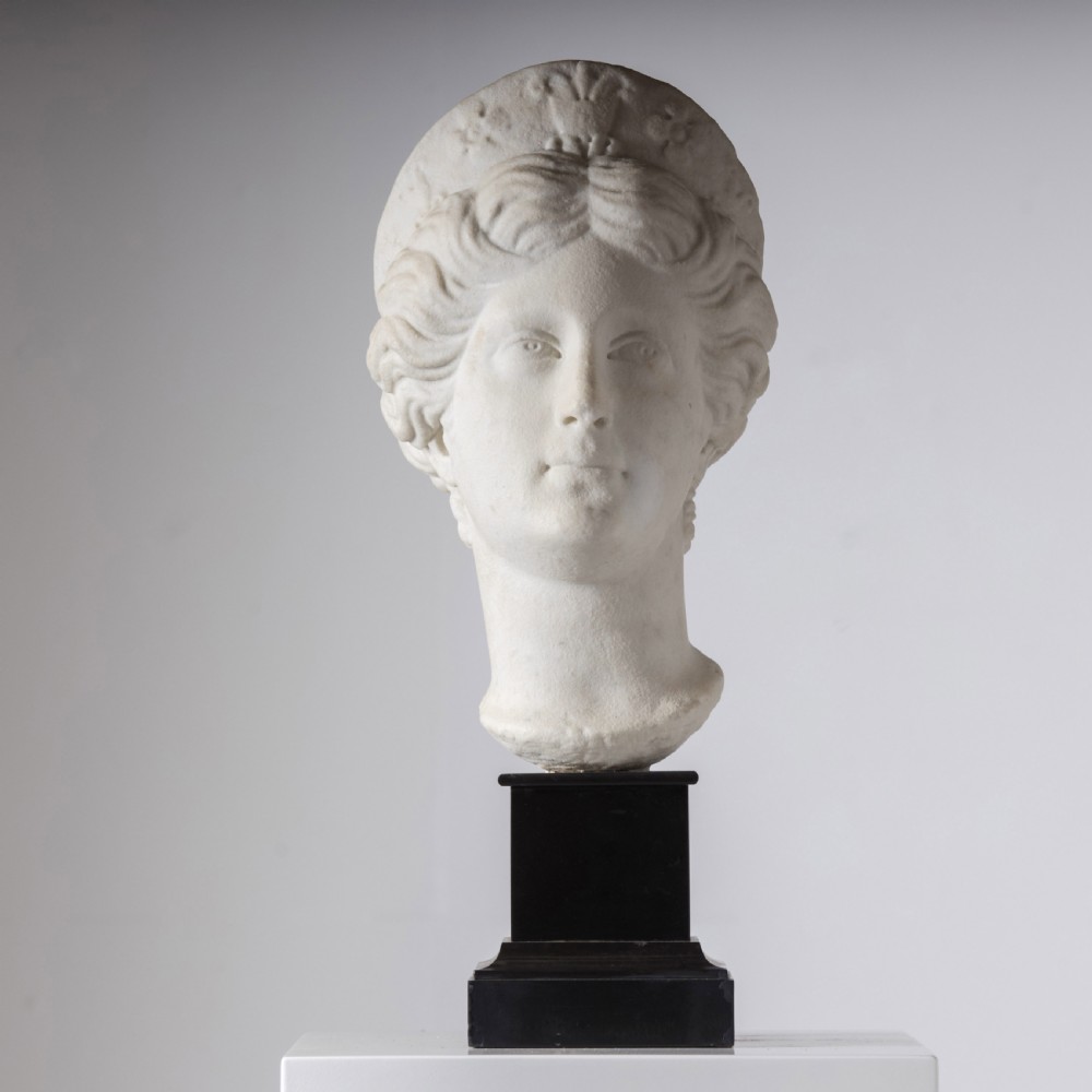 An off-white carved marble bust depicting the goddess Juno with wavy hair and a diadem, mounted on a square black marble plinth.