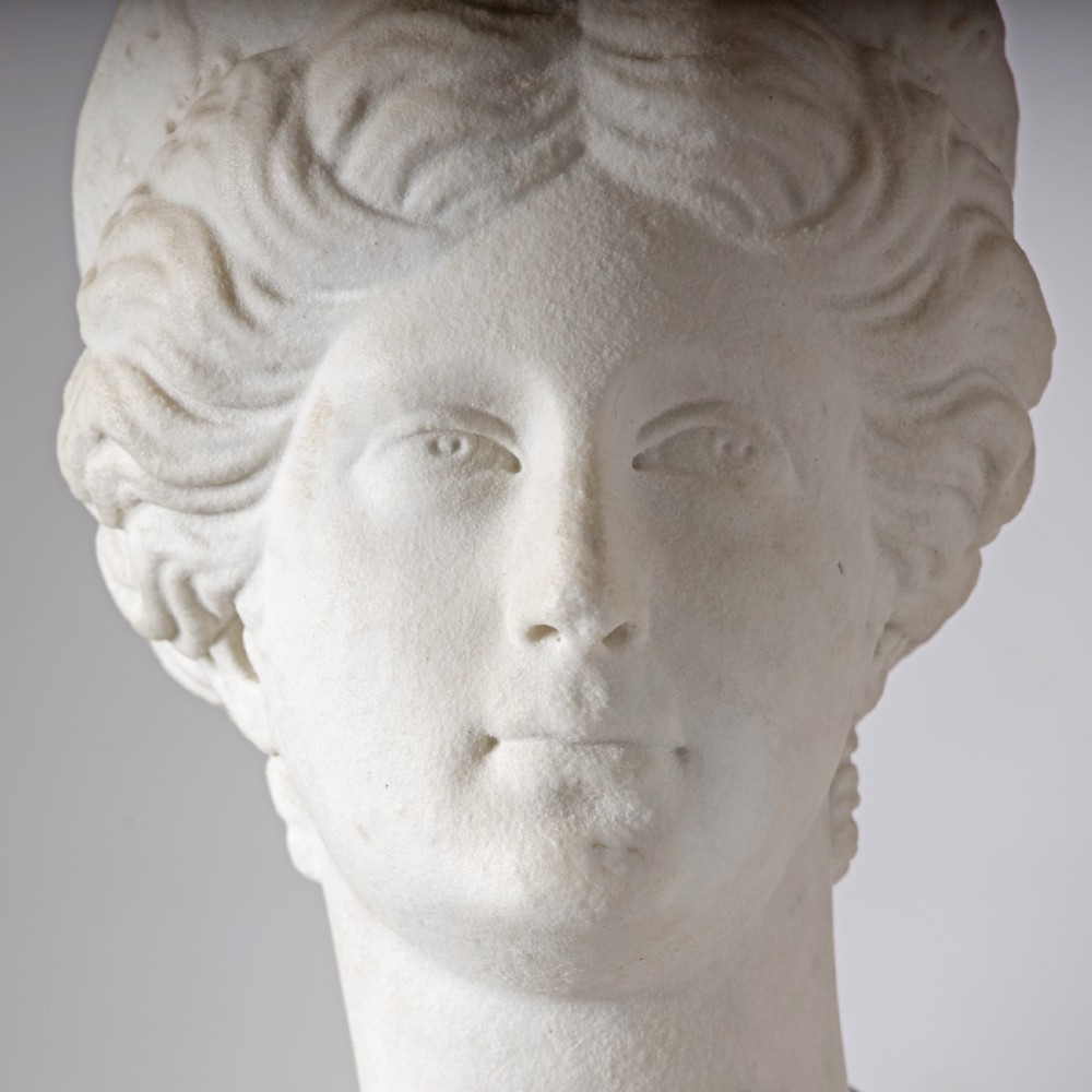 An off-white carved marble bust depicting the goddess Juno with wavy hair and a diadem, mounted on a square black marble plinth. View IV