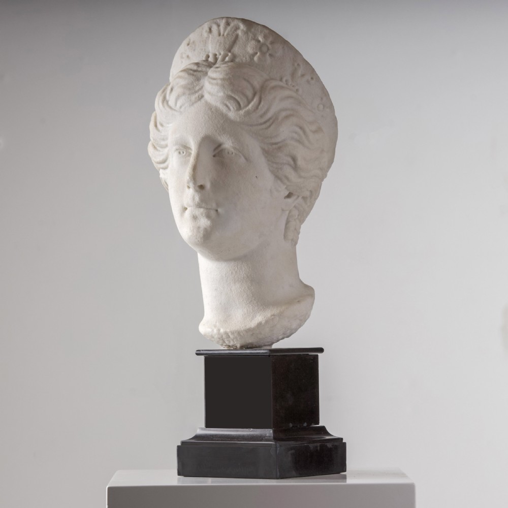 An off-white carved marble bust depicting the goddess Juno with wavy hair and a diadem, mounted on a square black marble plinth. View VI
