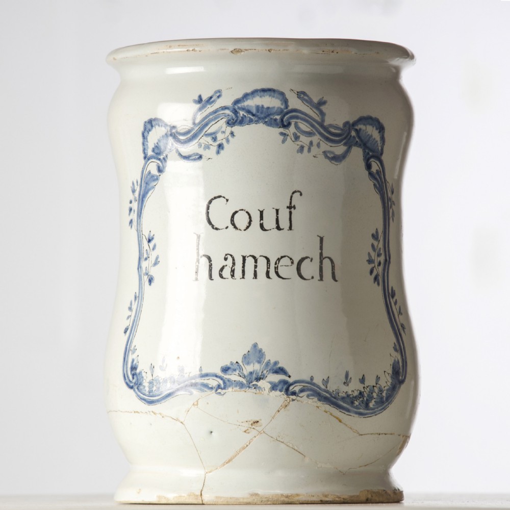 A cylindrical 19th-century tin-glazed ceramic pharmacy jar featuring a blue painted scrollwork cartouche with Latin text.