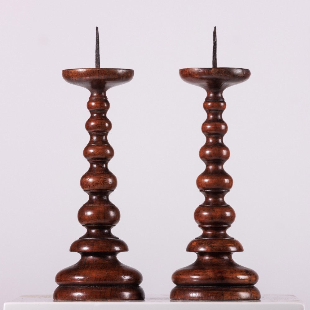 A pair of 18th-century turned dark wood pricket candlesticks featuring iron spikes and stepped circular bases.