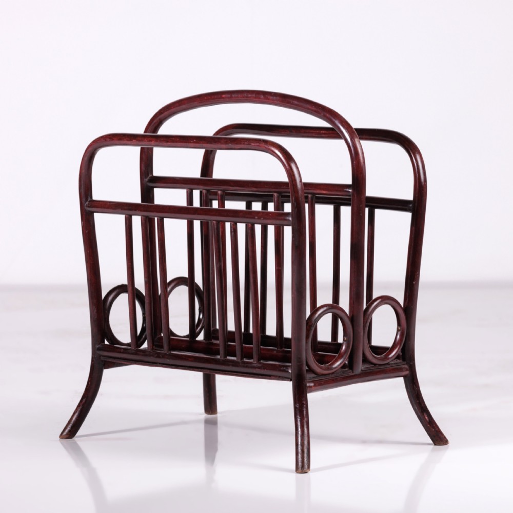 A dark reddish-brown bentwood magazine rack featuring a central arched carrying handle, vertical spindles, and circular bentwood side accents.