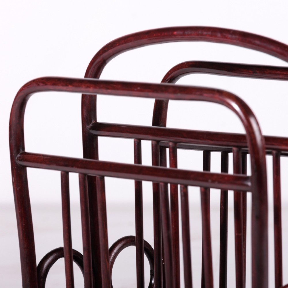 A dark reddish-brown bentwood magazine rack featuring a central arched carrying handle, vertical spindles, and circular bentwood side accents. View V