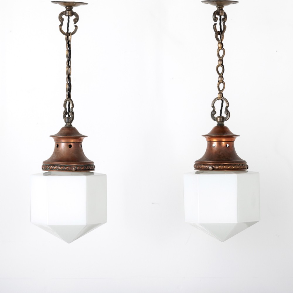 A pair of 1930s Art Deco pendant lights featuring faceted white opal glass hexagonal shades and flared copper top galleries with hanging loop attachments. View II