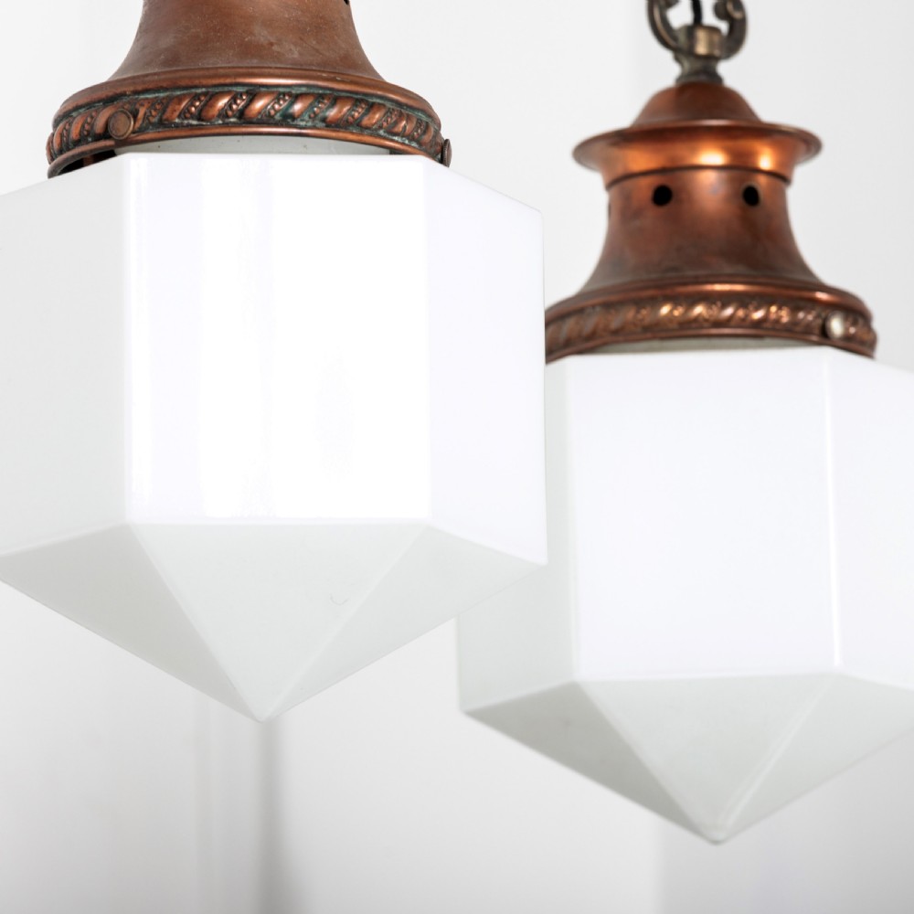 A pair of 1930s Art Deco pendant lights featuring faceted white opal glass hexagonal shades and flared copper top galleries with hanging loop attachments. View IV