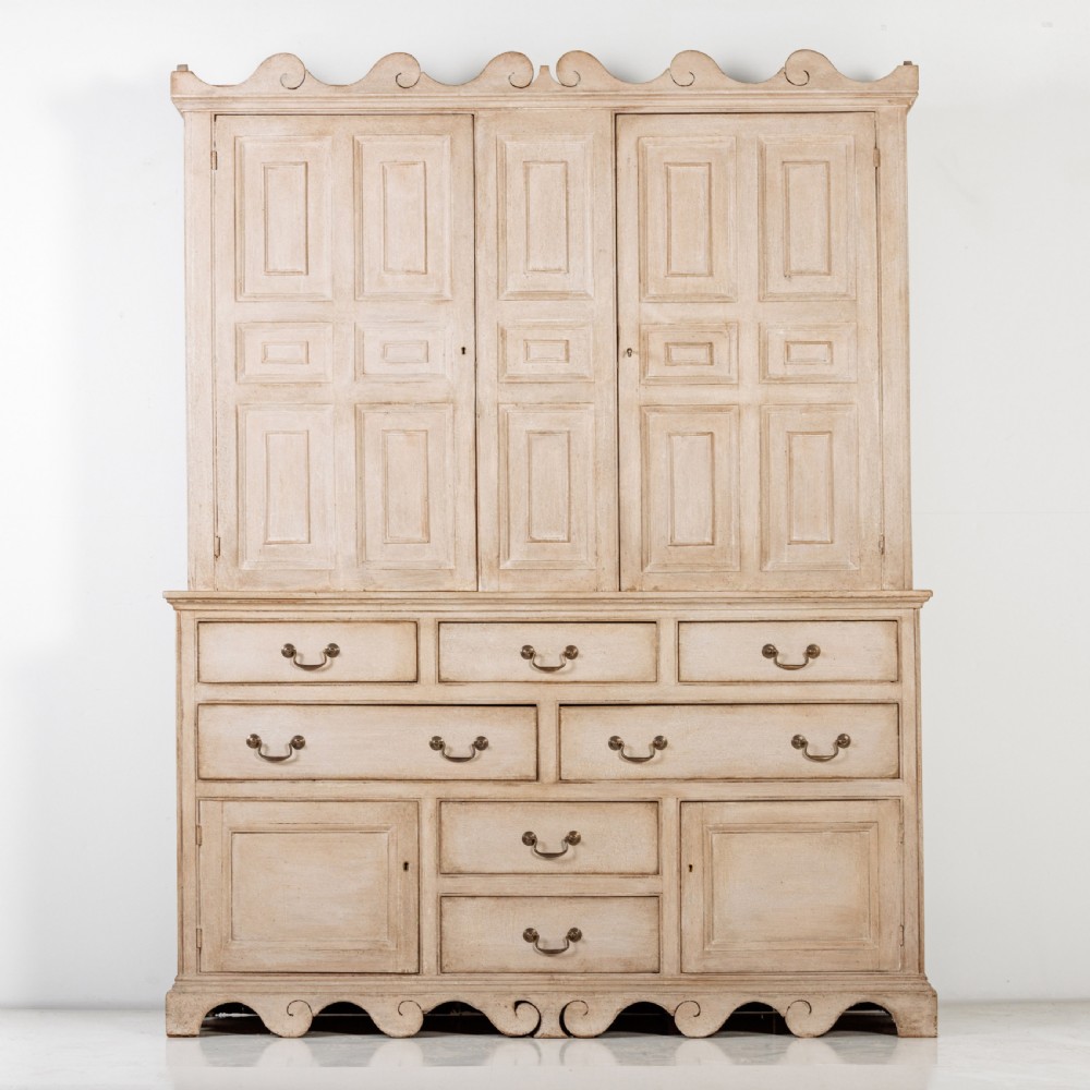 A large 19th-century pale timber dresser featuring a scalloped cornice, panelled upper cupboard doors, and multiple drawers with brass drop handles above a scalloped base.