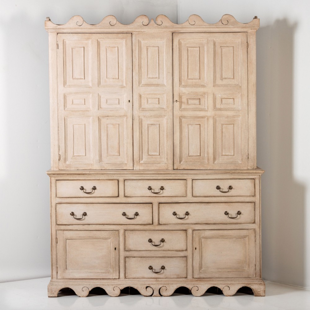 A large 19th-century pale timber dresser featuring a scalloped cornice, panelled upper cupboard doors, and multiple drawers with brass drop handles above a scalloped base. View II